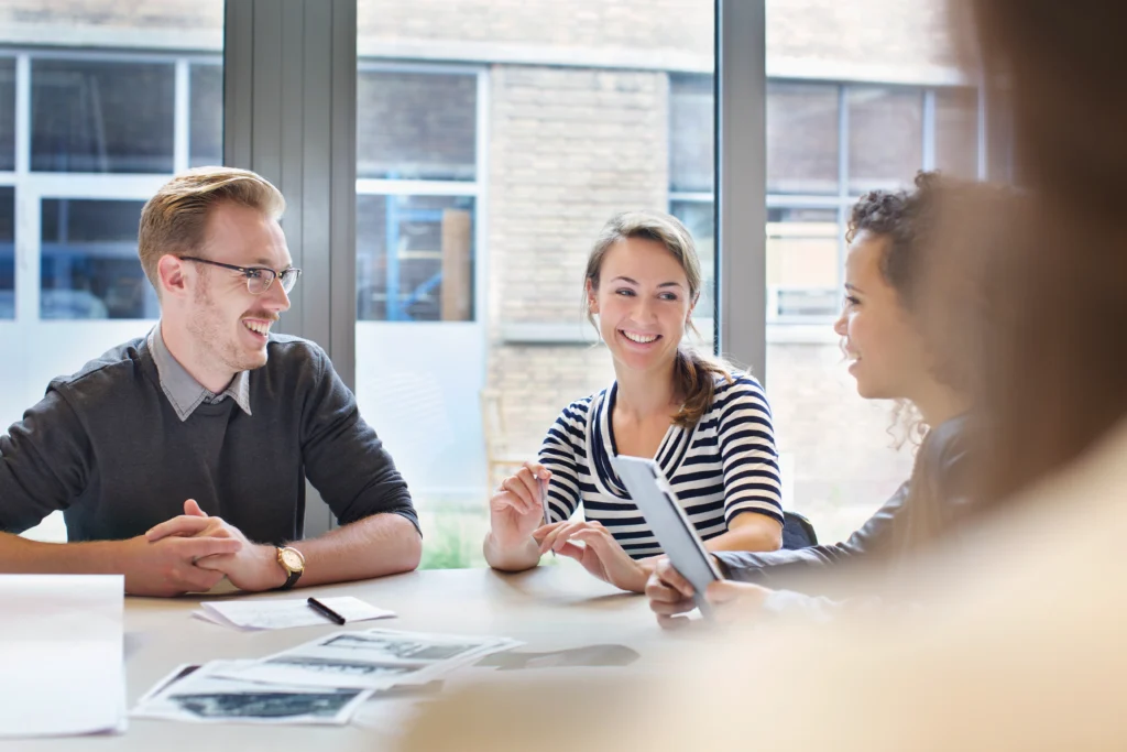 Tres profesionales discuten ideas en una mesa, recibiendo asesoría empresarial en un entorno de trabajo moderno.