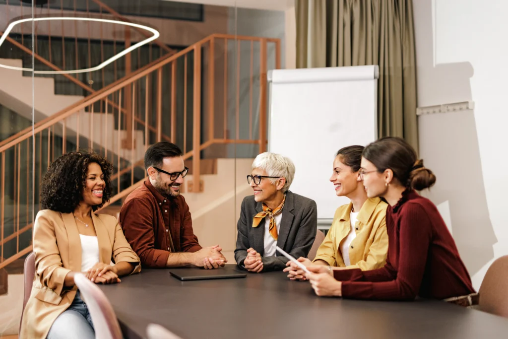 Un equipo de profesionales sonríe en una reunión, ejemplificando una comunicación organizacional positiva y fluida.