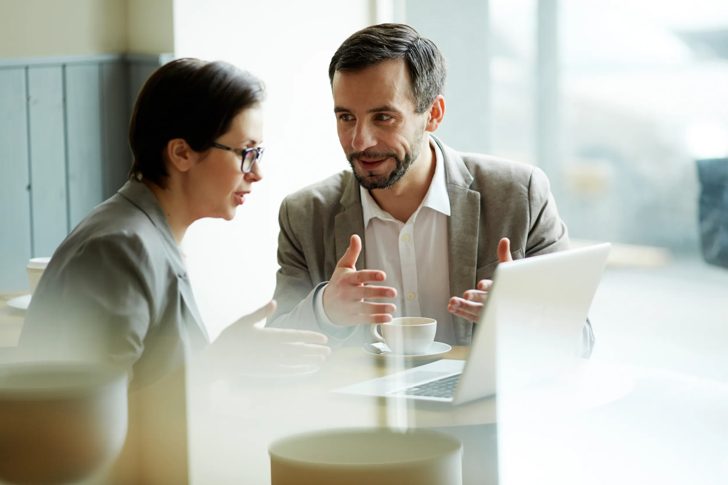 Explicación práctica sobre qué es la consultoría empresarial Dos profesionales en una cafetería analizando en una laptop qué es la consultoría empresarial y cómo implementarla.